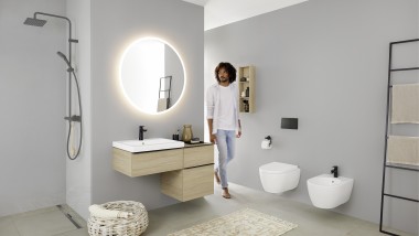 Homme entrant dans une salle de bains équipée d’un lavabo, d’un WC, d’un bidet et de meubles de la collection Geberit iCon.